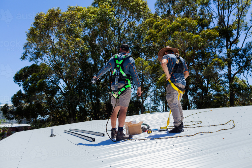 Electrician tradesmen workers on house roof discussing installing solar panel system together - Australian Stock Image