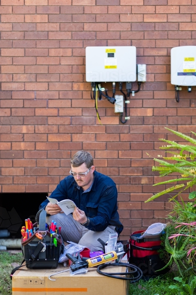 Electrician tradie reading solar power installation manual - Australian Stock Image