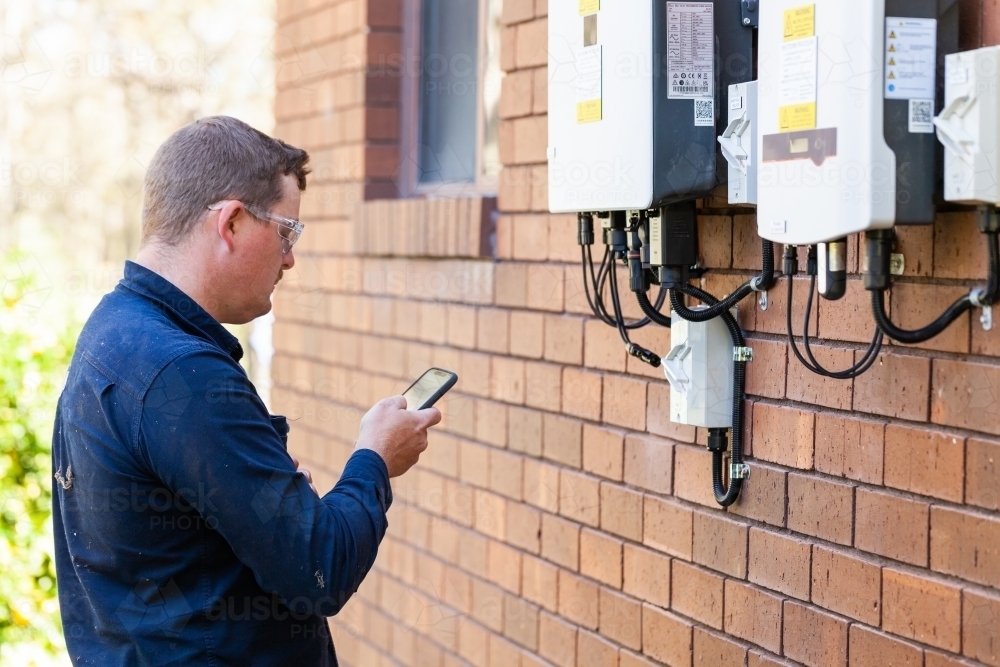 Electrician using mobile phone device to troubleshoot - Australian Stock Image