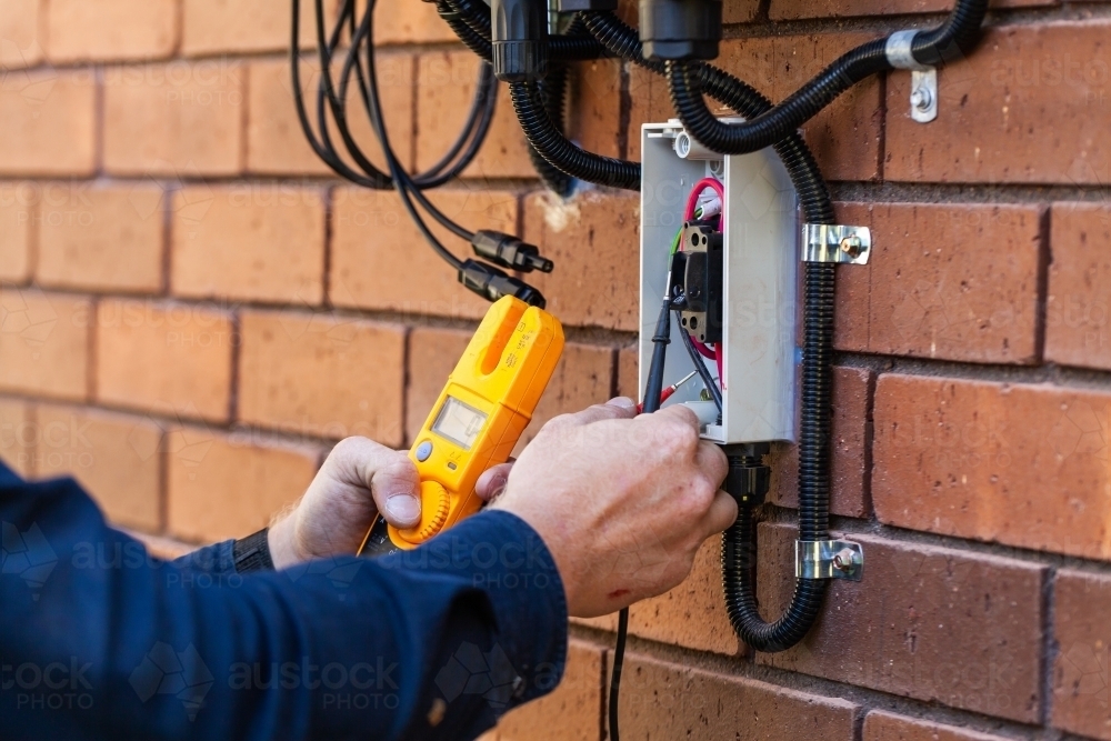 Electrician using multimeter tool to check power in solar system installation - Australian Stock Image