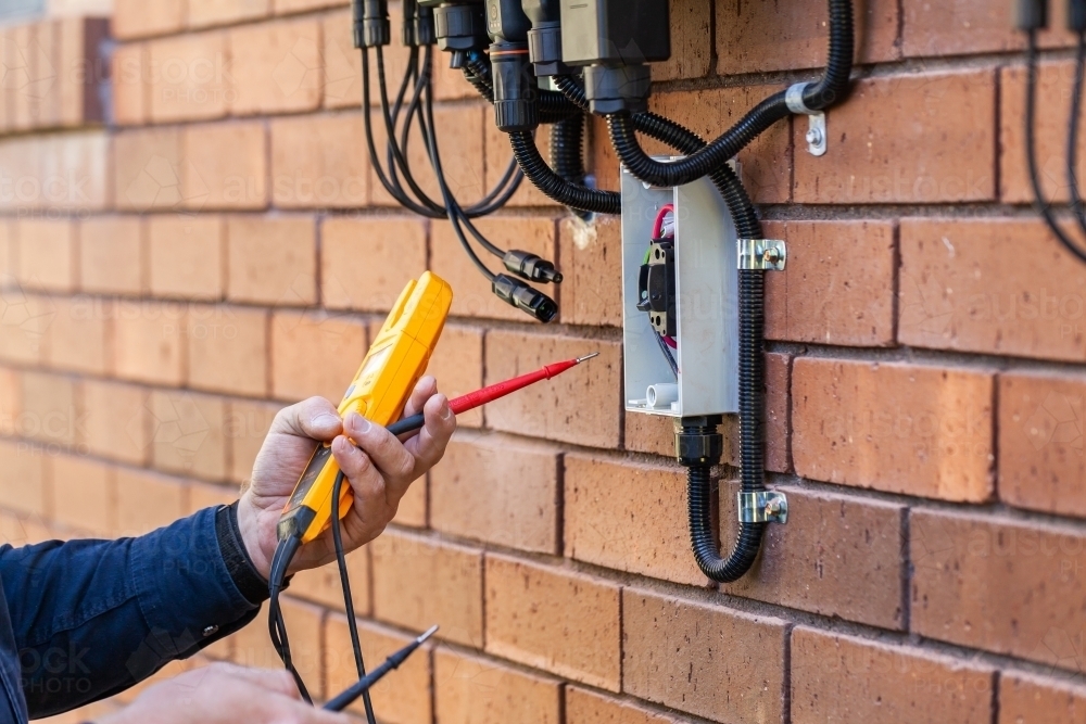 Electrician using multimeter tool to check power in solar system installation - Australian Stock Image