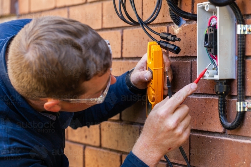 Electrician using multimeter tool to check power in solar system installation - Australian Stock Image