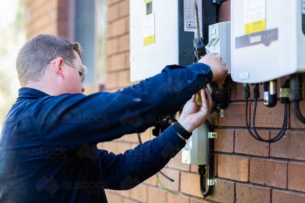 Electrician using silicone glue gun to make electrical wiring into house weatherproof - Australian Stock Image