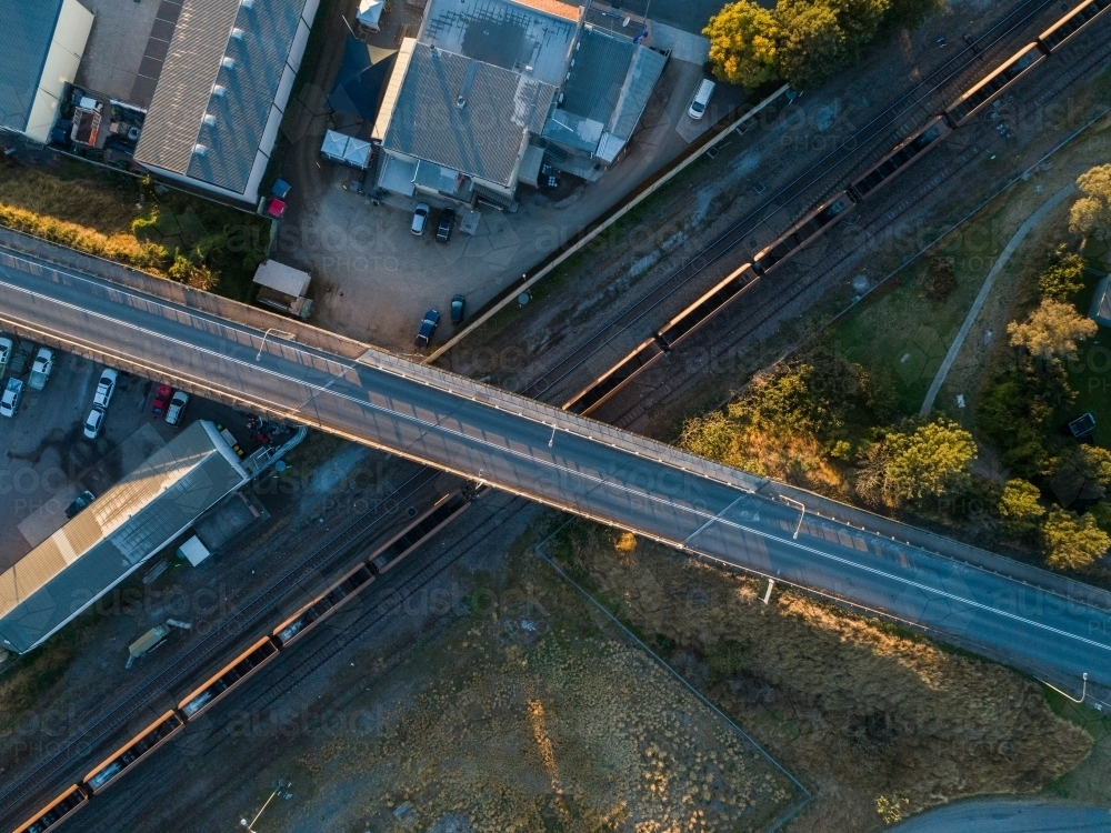 Empty coal train passing under bridge over railway seen from top down aerial view - Australian Stock Image