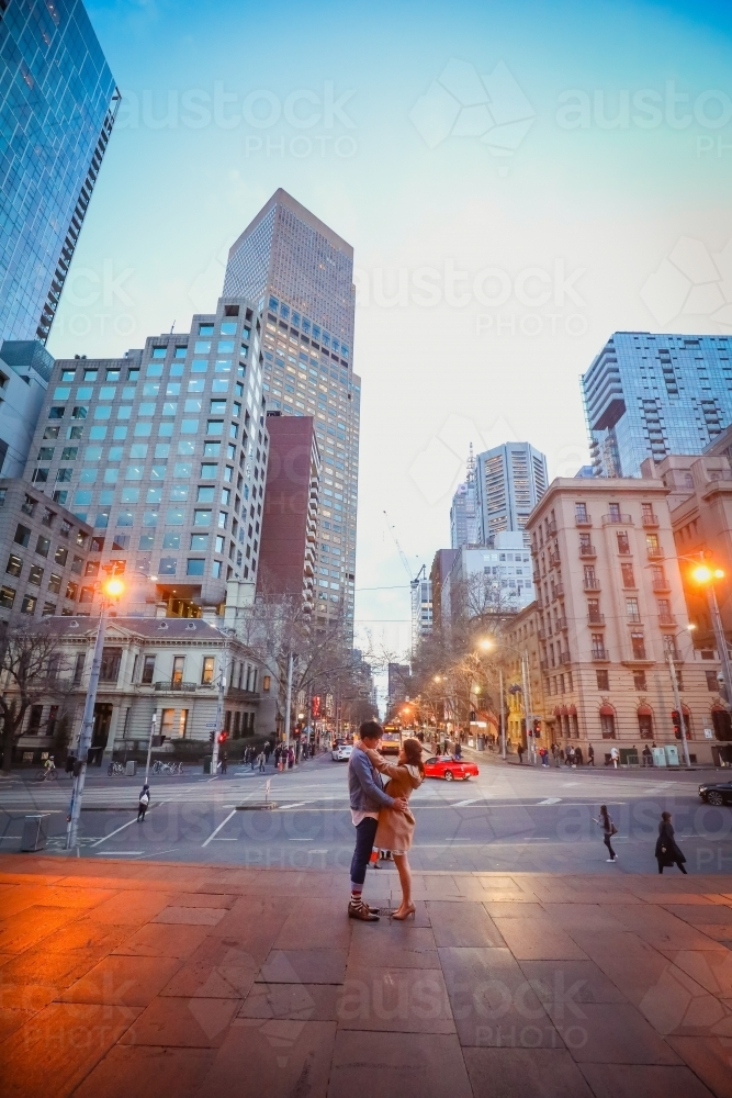 Engaged couple embracing in the city with Melbourne cityscape in background at night - Australian Stock Image