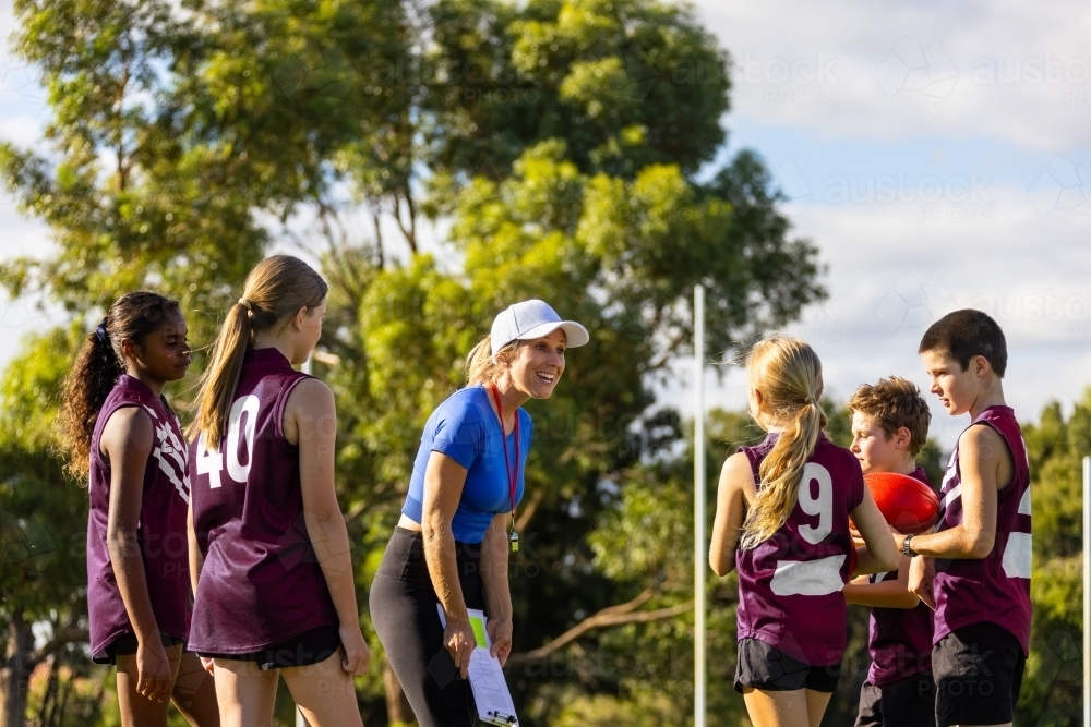 enthusiastic female coach encouraging her young football team - Australian Stock Image