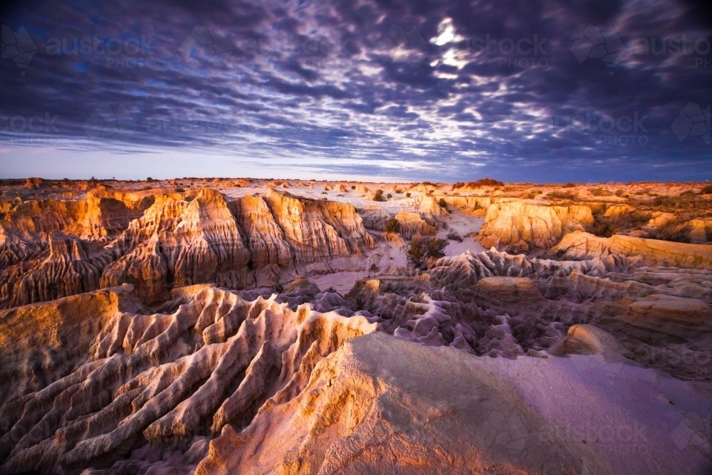 Eroded landscape of middens and creek beds at sunset - Australian Stock Image