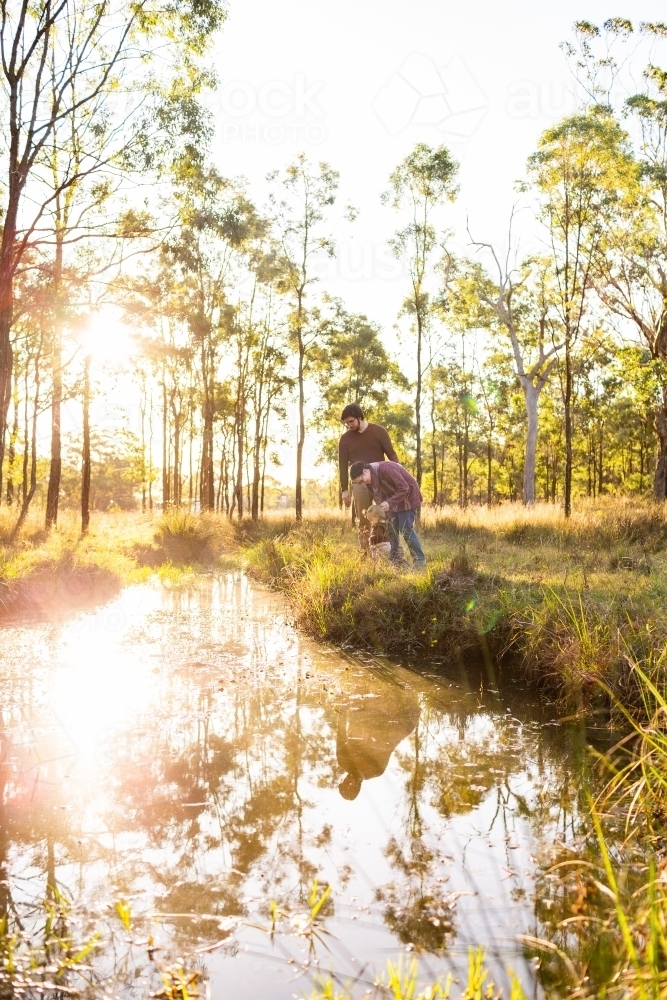 Evening sunlight reflecting of water in creek paddock with family standing beside water - Australian Stock Image