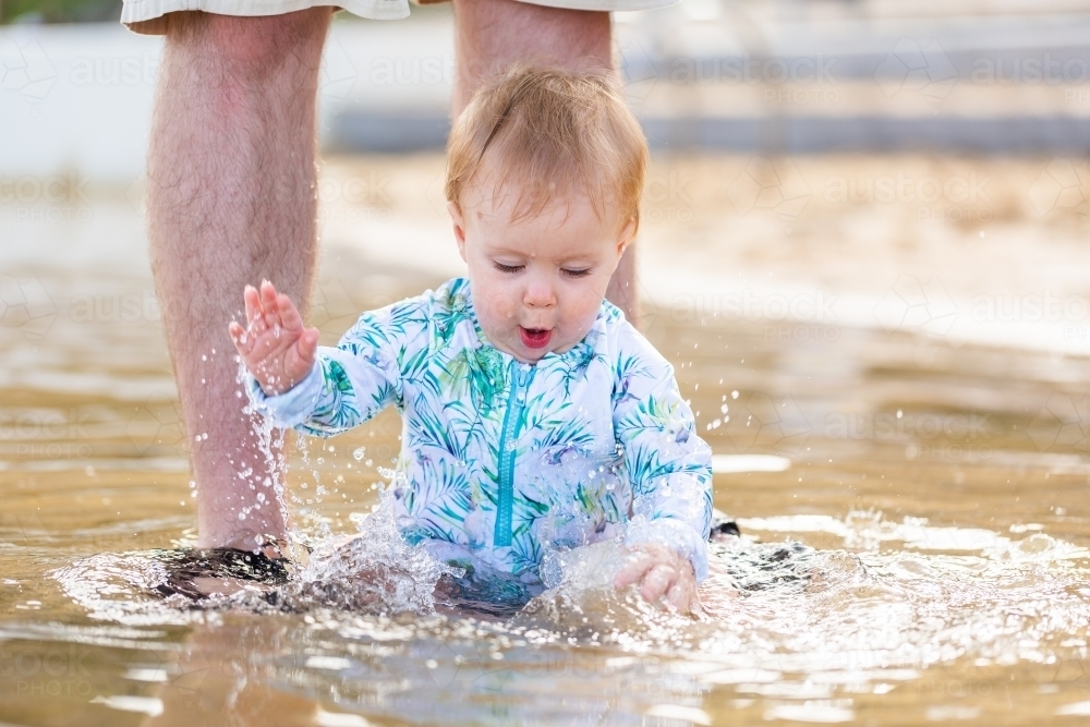 Excited baby girl splashing in water at beach on holiday - Australian Stock Image