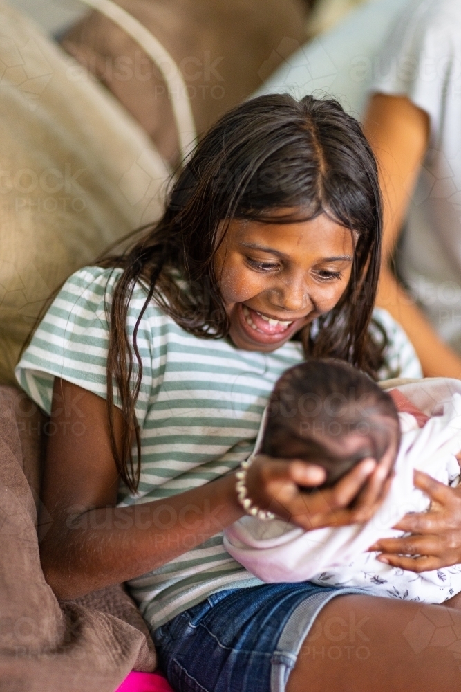 excited young girl holding her newborn baby sister - Australian Stock Image