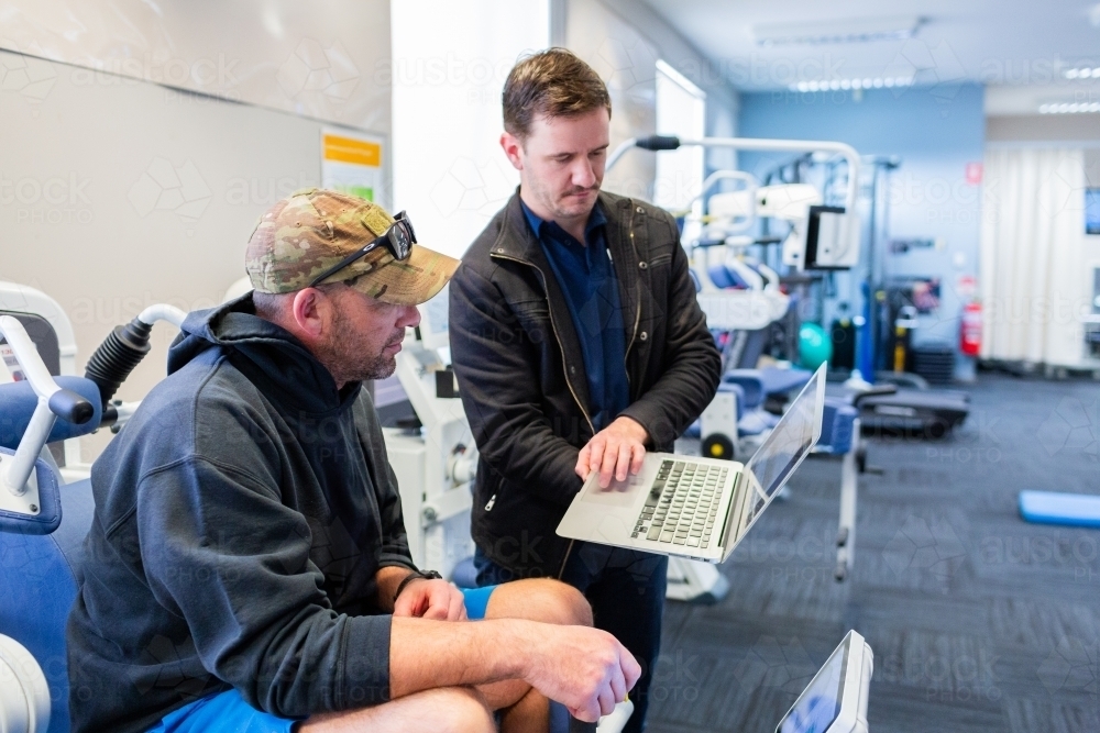 exercise therapy equipment at physiotherapy clinic with men discussing progress - Australian Stock Image