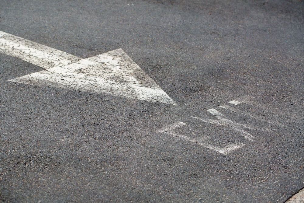 Faded white arrow painted on bitumen road - Australian Stock Image