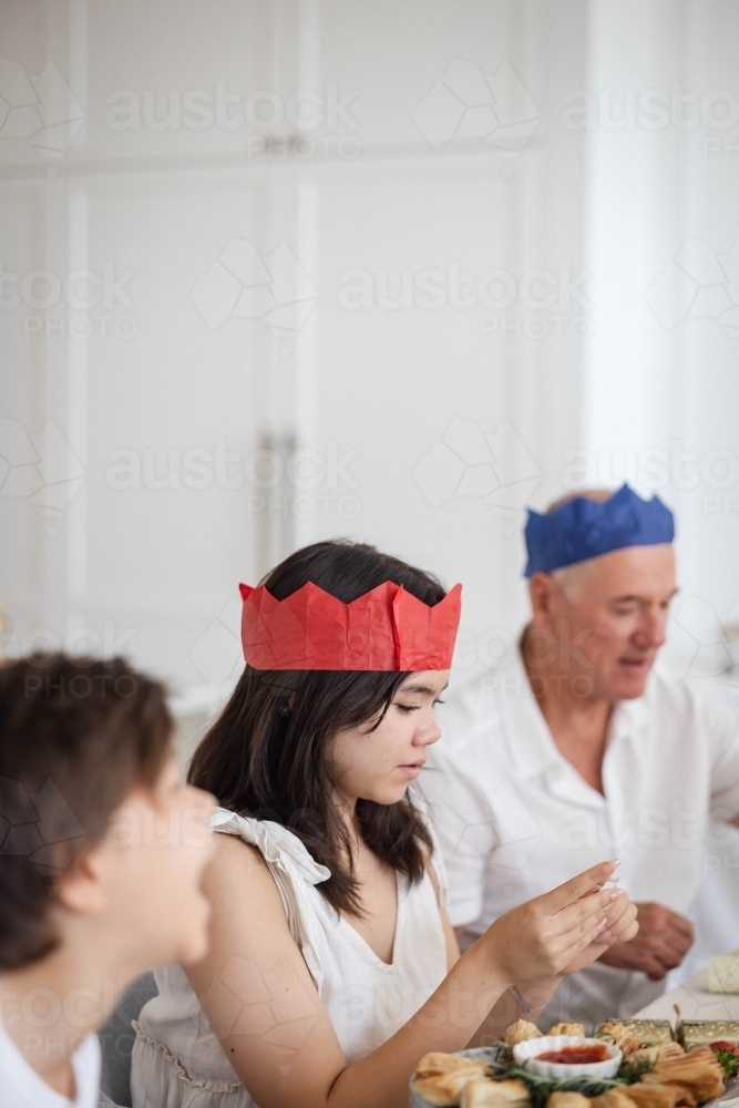 Family at Christmas table with girl reading bon-bon joke - Australian Stock Image