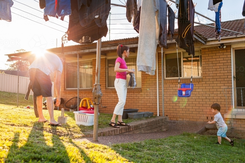 Family getting in washing off clothesline in backyard together with sunlight - Australian Stock Image