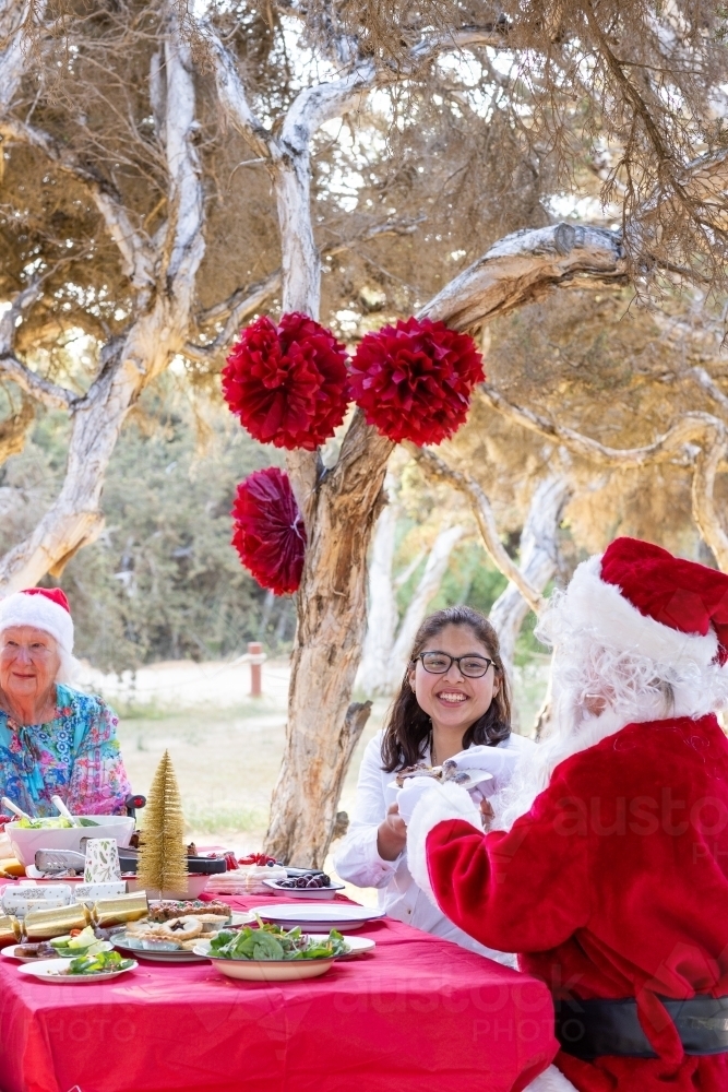 Image of family having Christmas lunch at a table in a park with man ...