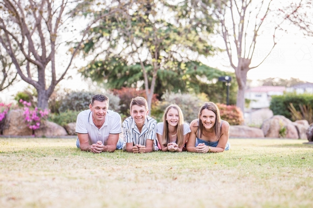 Family of four lying together on grass looking and smiling - Australian Stock Image