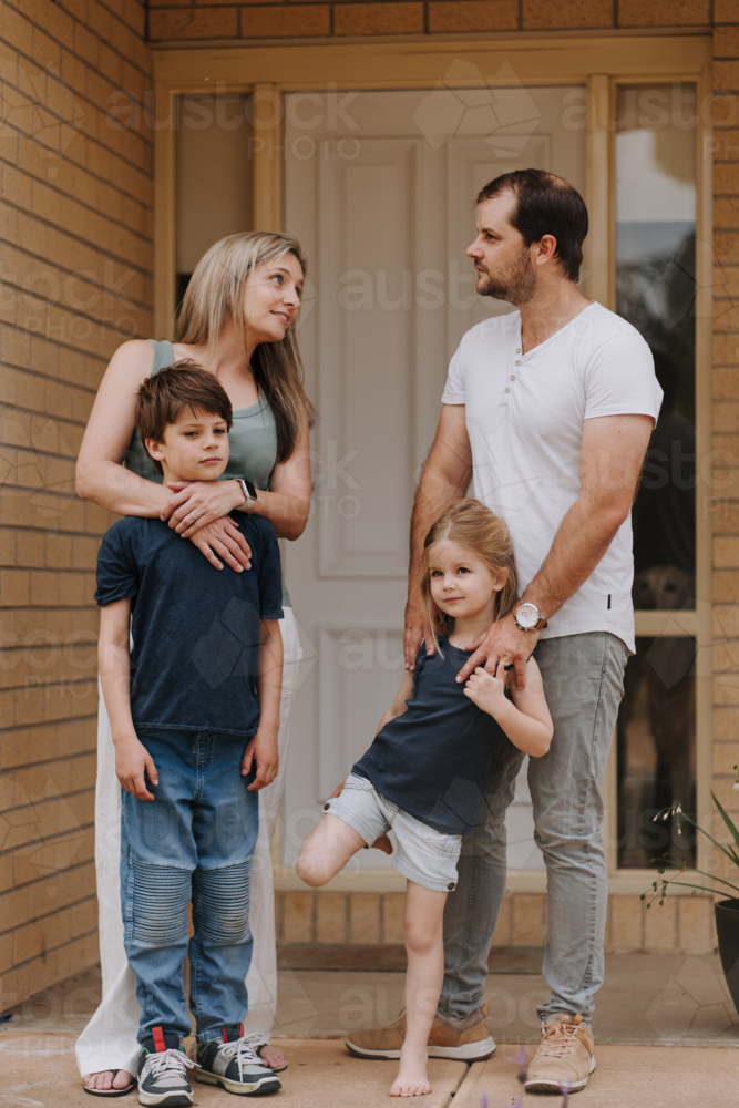 Family of four standing in front of their house. - Australian Stock Image