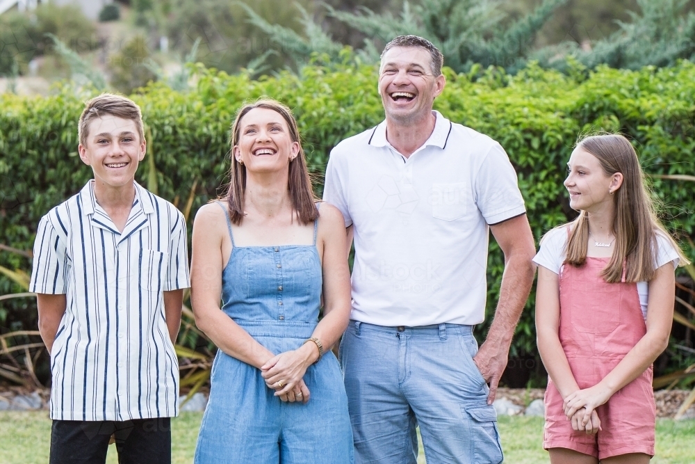 Family of four standing together in garden laughing - Australian Stock Image