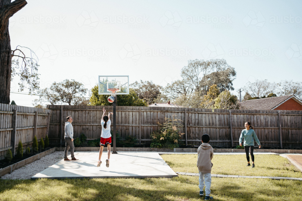 Family playing basketball in their yard. - Australian Stock Image