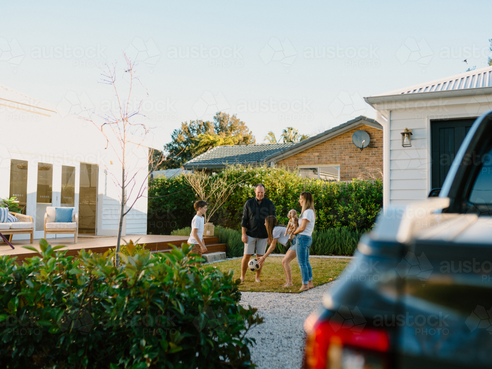 Family playing with a soccer ball in their yard. - Australian Stock Image