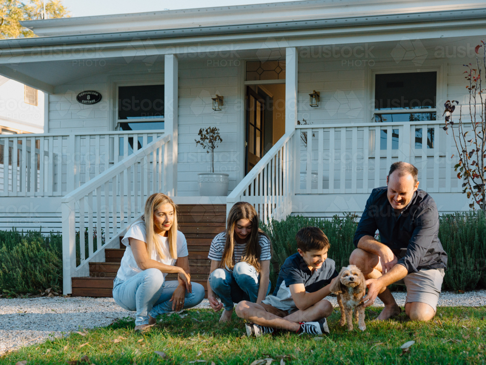 Family playing with their dog in the front yard of the house. - Australian Stock Image