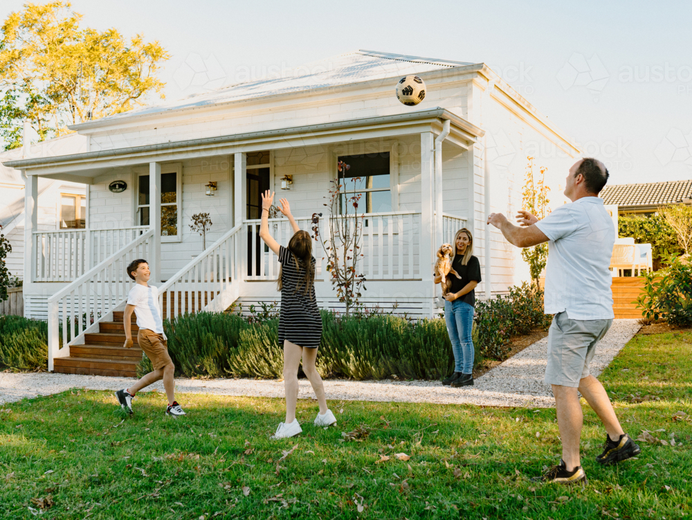 Family tossing a soccer ball inside their yard. - Australian Stock Image