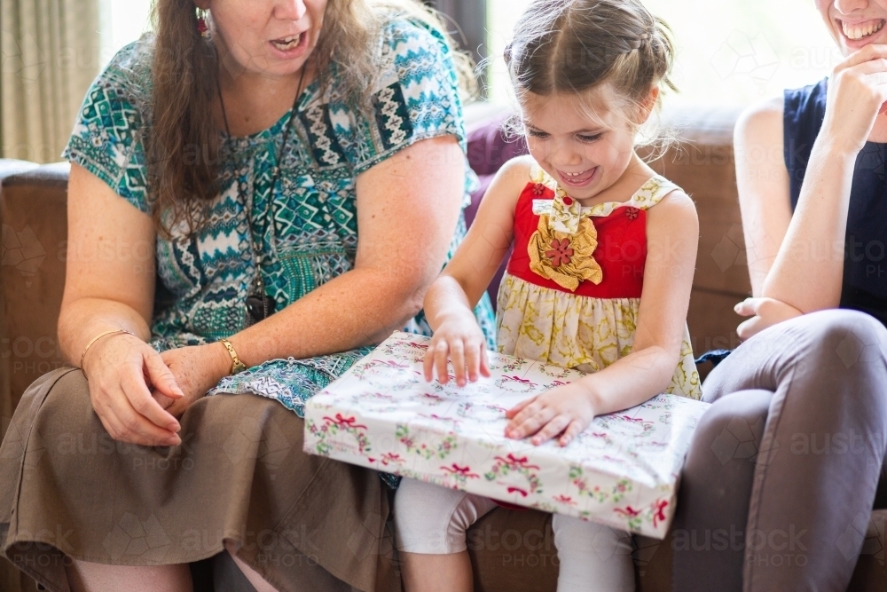 Family unwrapping Christmas gifts together, little girl with big gift - Australian Stock Image