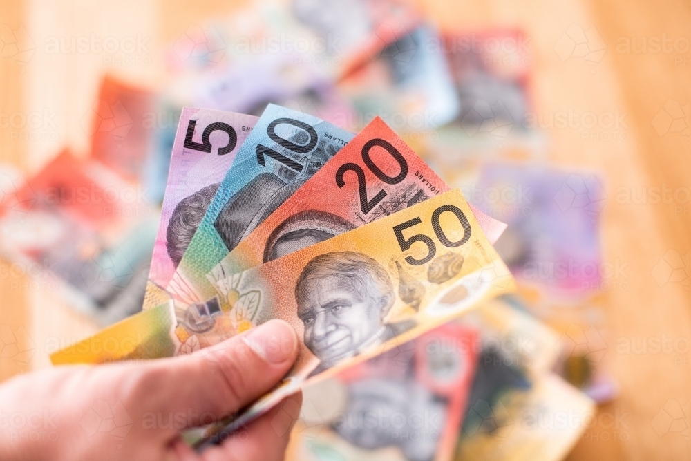 fan of cash in hand and more money in the background - Australian Stock Image