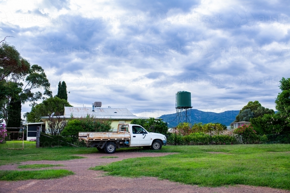 Farm ute vehicle parked outside of homestead yard with water tank - Australian Stock Image