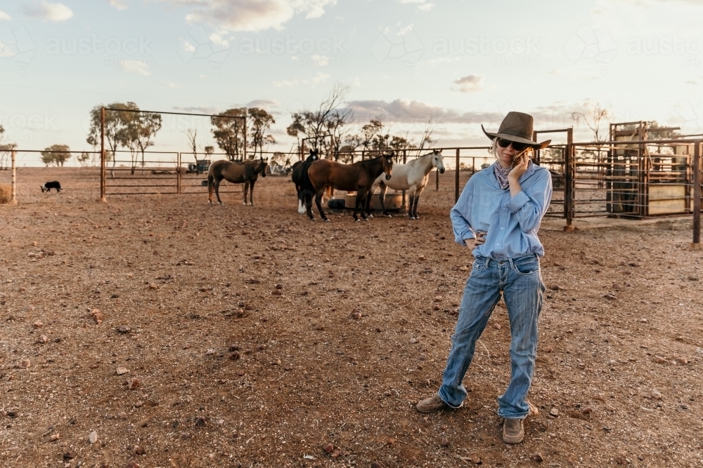 Farm woman using mobile phone in the horse yard - Australian Stock Image