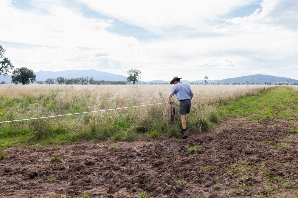 Farmer adjusting electric wire fencing on farm using rotational grazing land management for cattle - Australian Stock Image