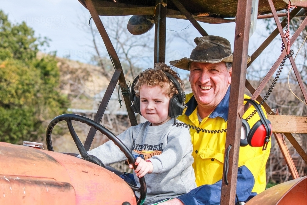 Farmer and young child driving tractor smiling - Australian Stock Image