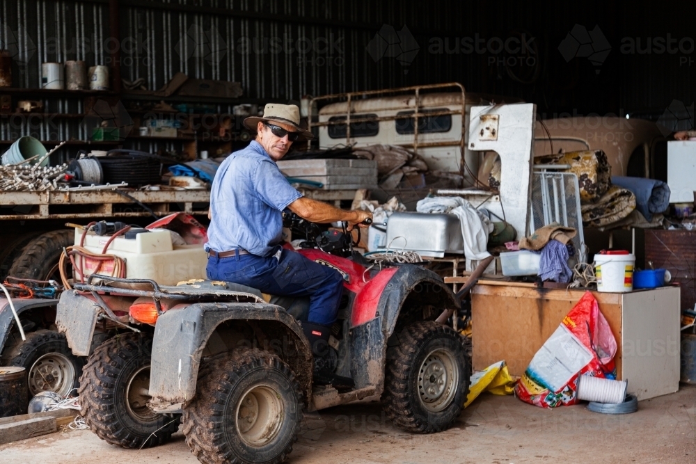 Farmer backing quad bike out of shed on farm - Australian Stock Image