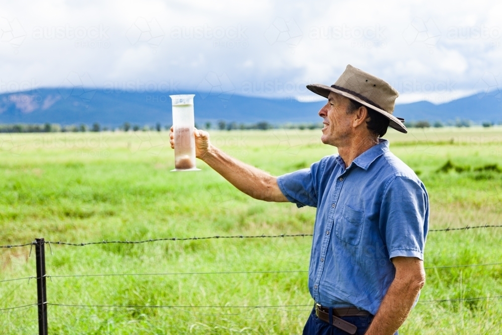 Farmer checking rain gauge after drought has broken and paddocks are green - Australian Stock Image