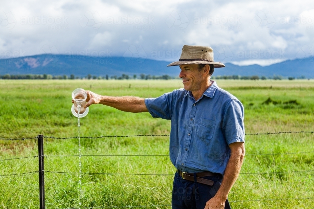 Farmer checking rain gauge after drought has broken and paddocks are green - Australian Stock Image