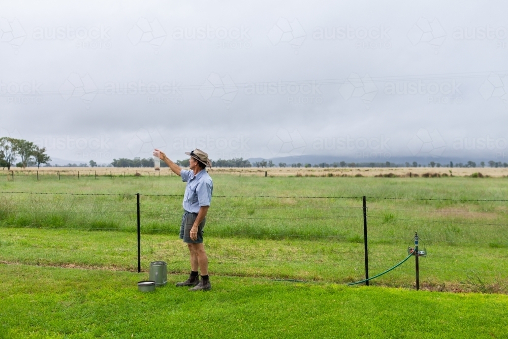 Farmer checking rain measurement on farm after rain storm has passed - Australian Stock Image