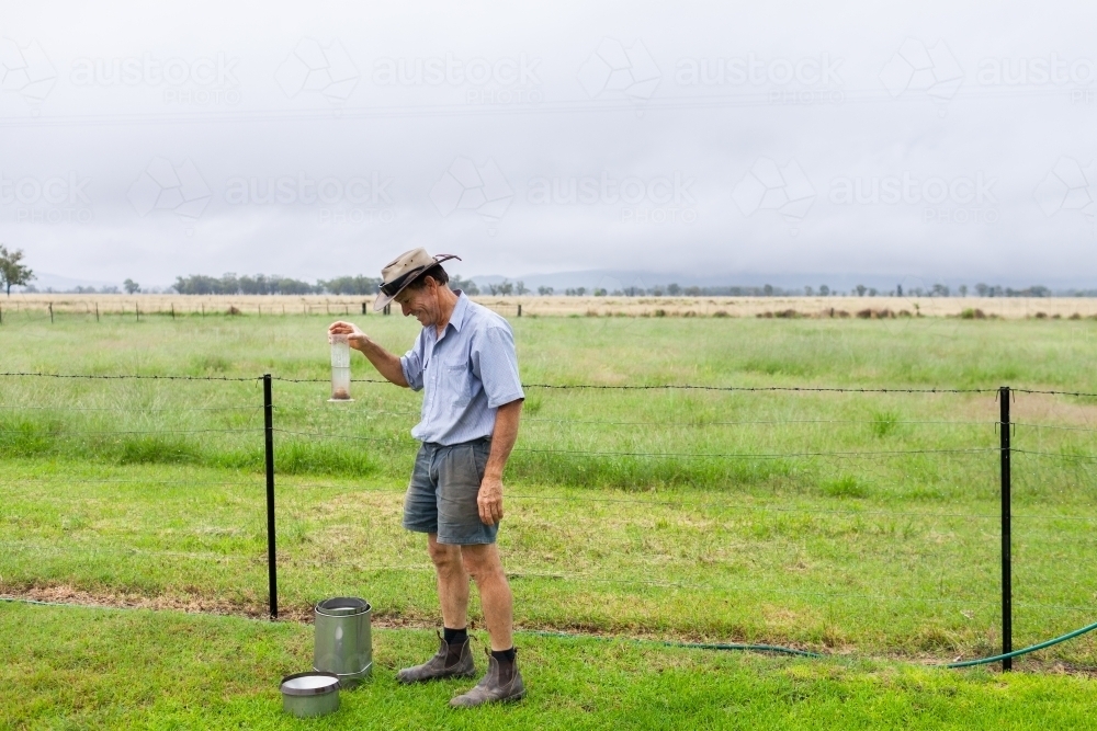 farmer checking rainfall as rain storm finishes - Australian Stock Image