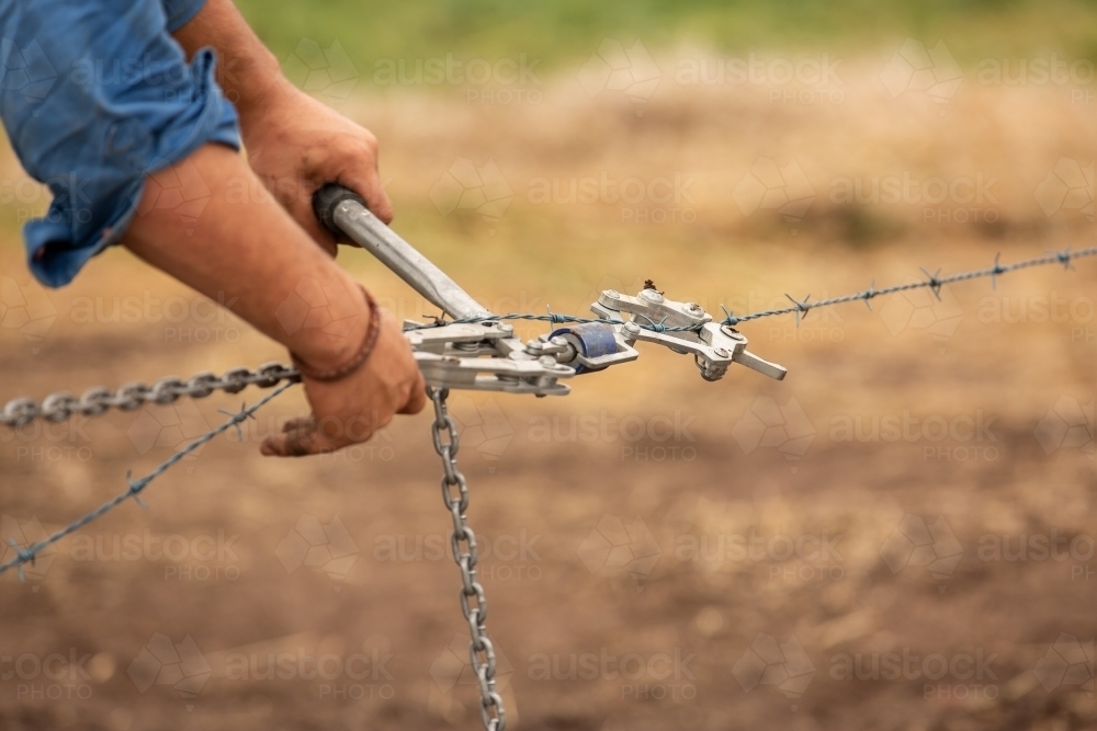 Farmer's hands working a wire strainer while fencing - Australian Stock Image