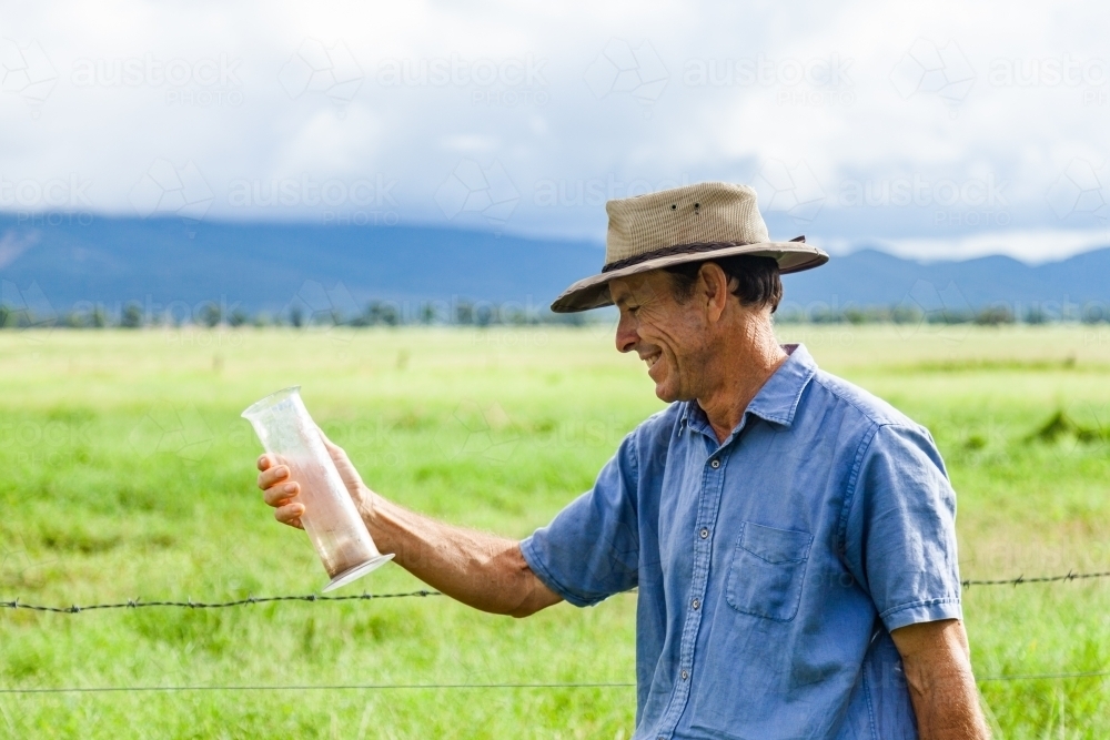 Farmer smiling at rain gauge measurement after storm - Australian Stock Image