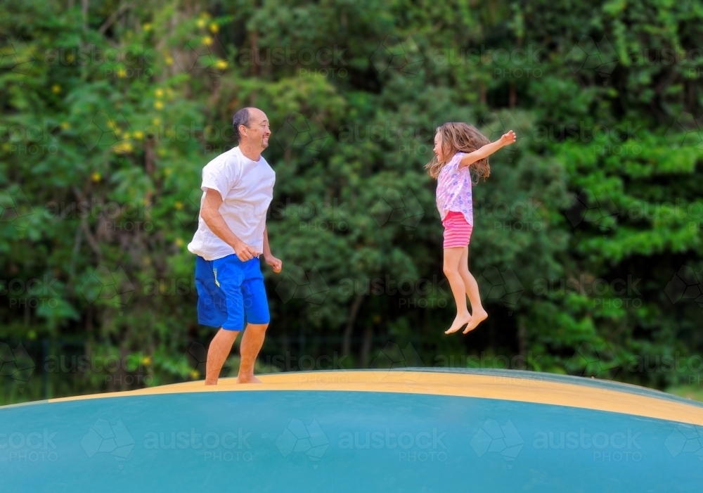 Father and daughter jumping on a jumping pillow having fun together - Australian Stock Image