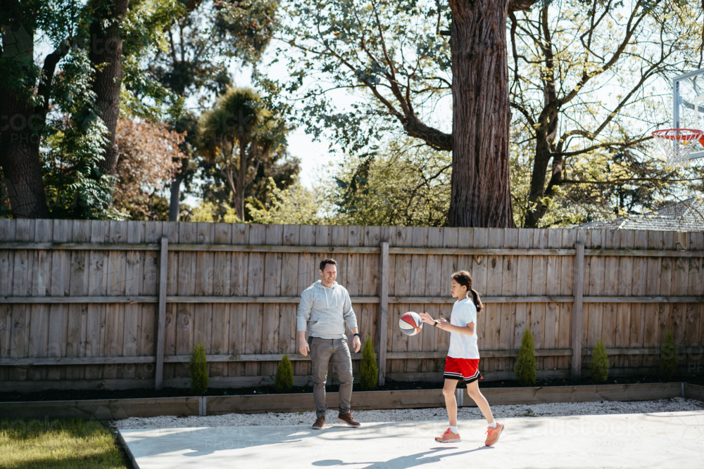 Father and daughter playing basketball in their yard. - Australian Stock Image