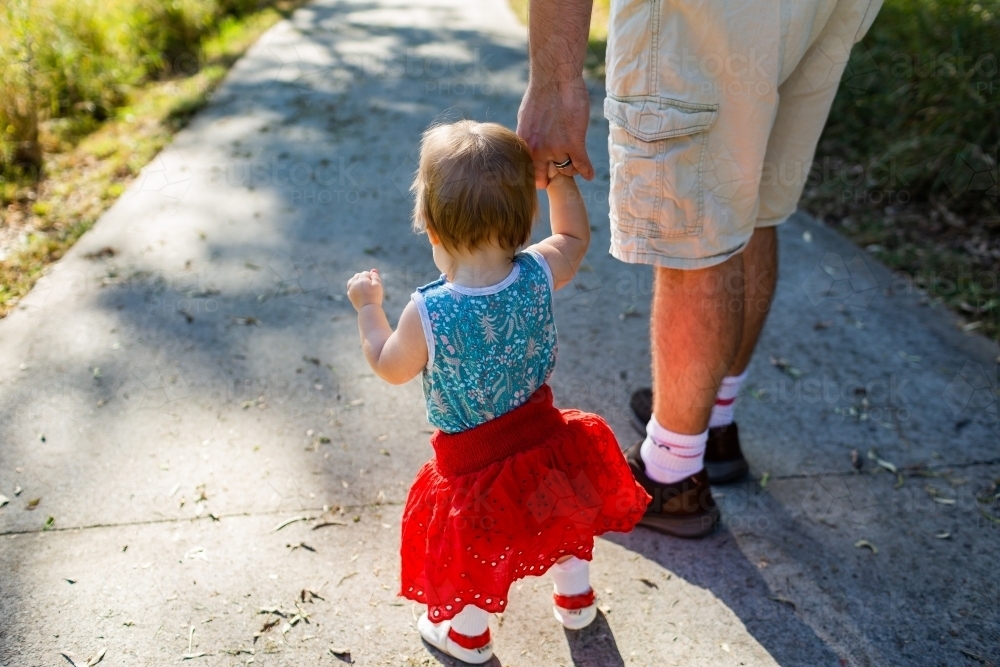 Father and daughter walking along path - toddler with red skirt on a walk with parent - Australian Stock Image