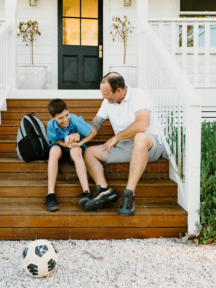 Father and son doing arm wrestling while sitting on the steps of their house. - Australian Stock Image