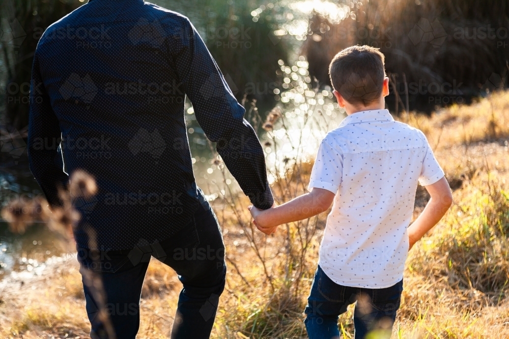Father and son holding hands on an adventure through the grass - Australian Stock Image