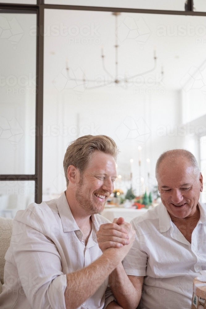 Father and son holding hands sitting together at home - Australian Stock Image