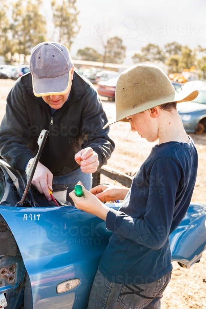 Father and son in wreckers pulling apart smashed car for parts - Australian Stock Image