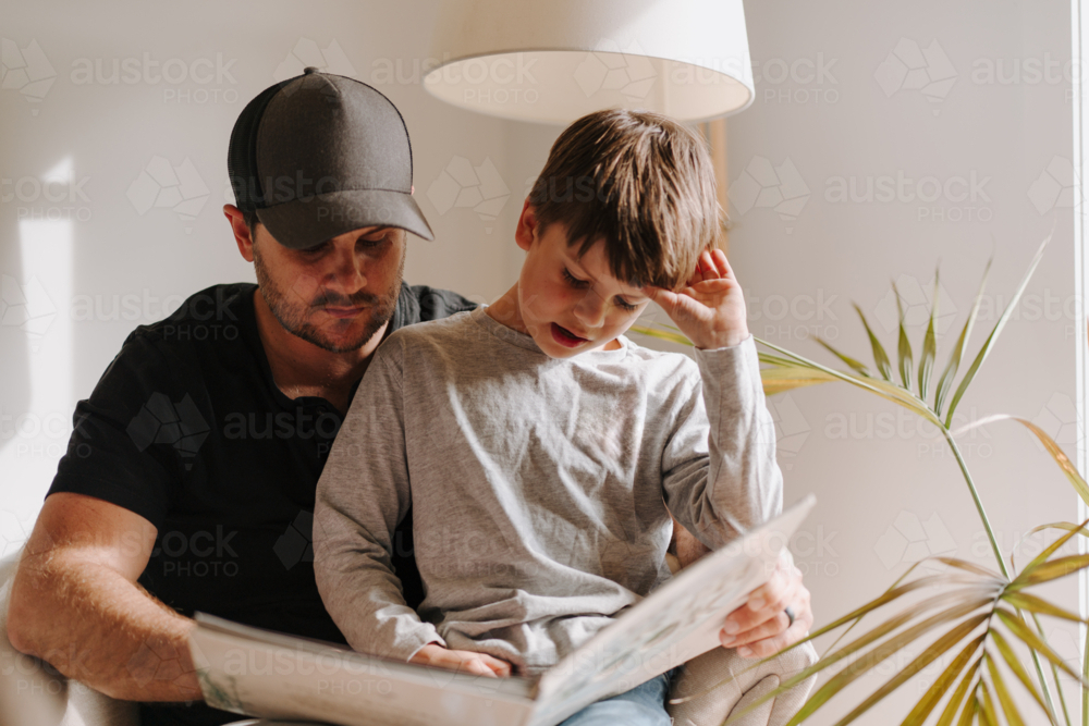 Father and son looking at an album while sitting on the couch. - Australian Stock Image