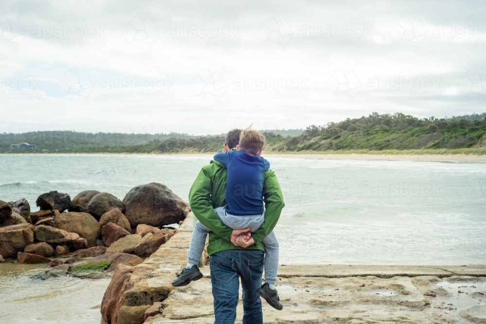 Father and son piggyback on ramp near ocean - Australian Stock Image