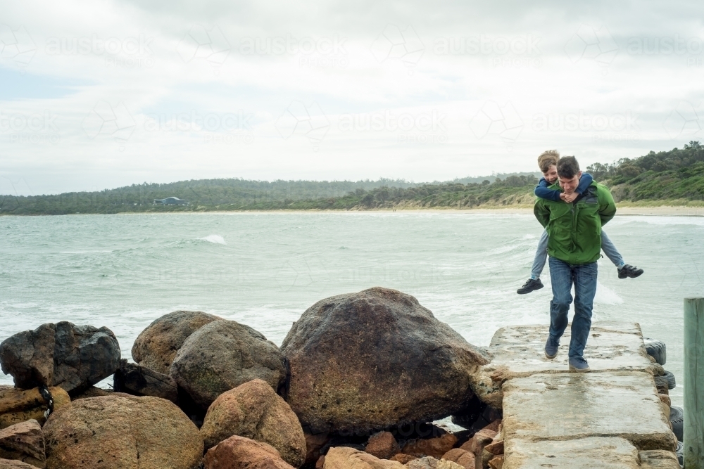 Father and son piggyback on ramp near ocean - Australian Stock Image