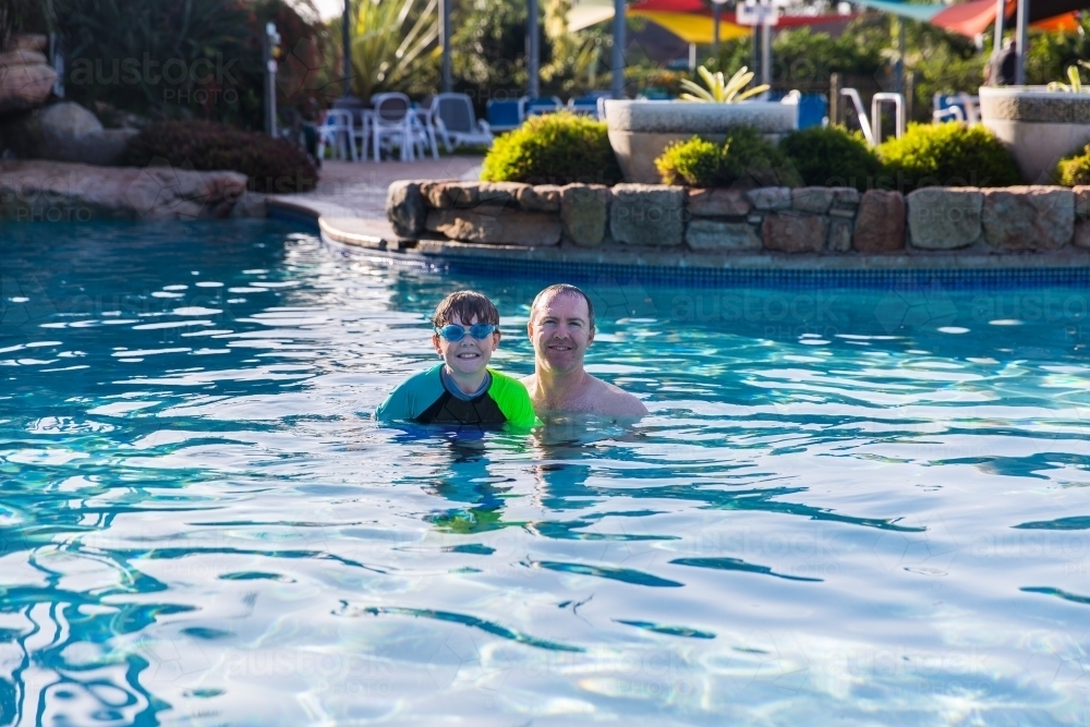 Father and son swimming in pool happy smiling on holidays - Australian Stock Image